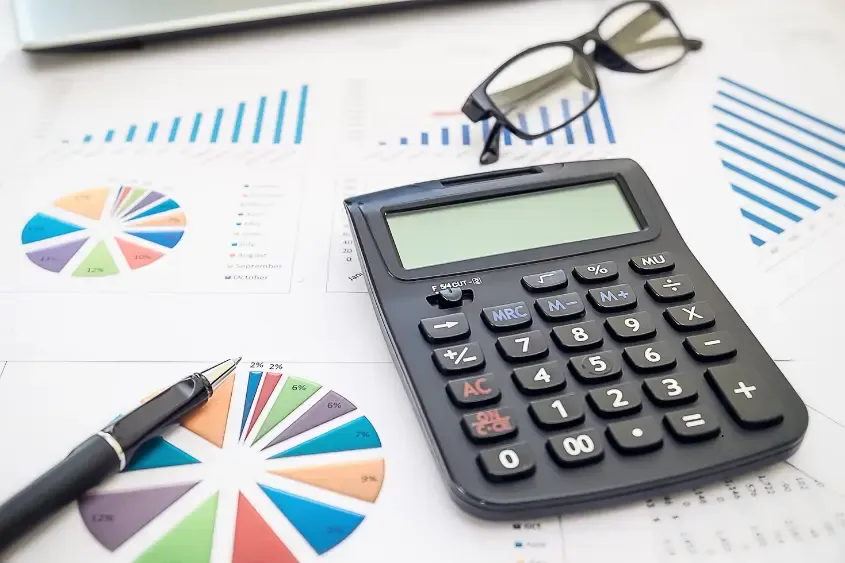Calculadora, caneta e óculos sobre relatórios com gráficos