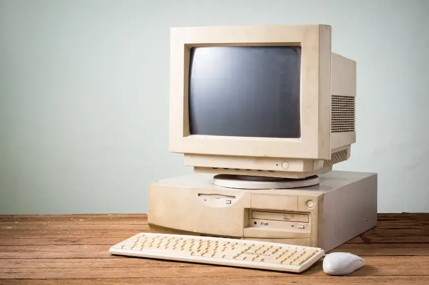 Computador antigo, de monitor de tubo, sobre uma mesa de madeira